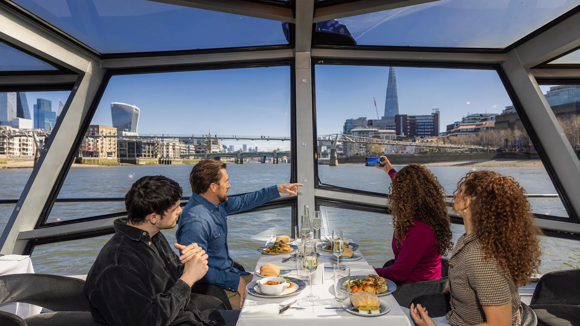 Guests at lunch under the glass roof of a Thames cruise boat with the Shard ahead, from the lunch cruise listing